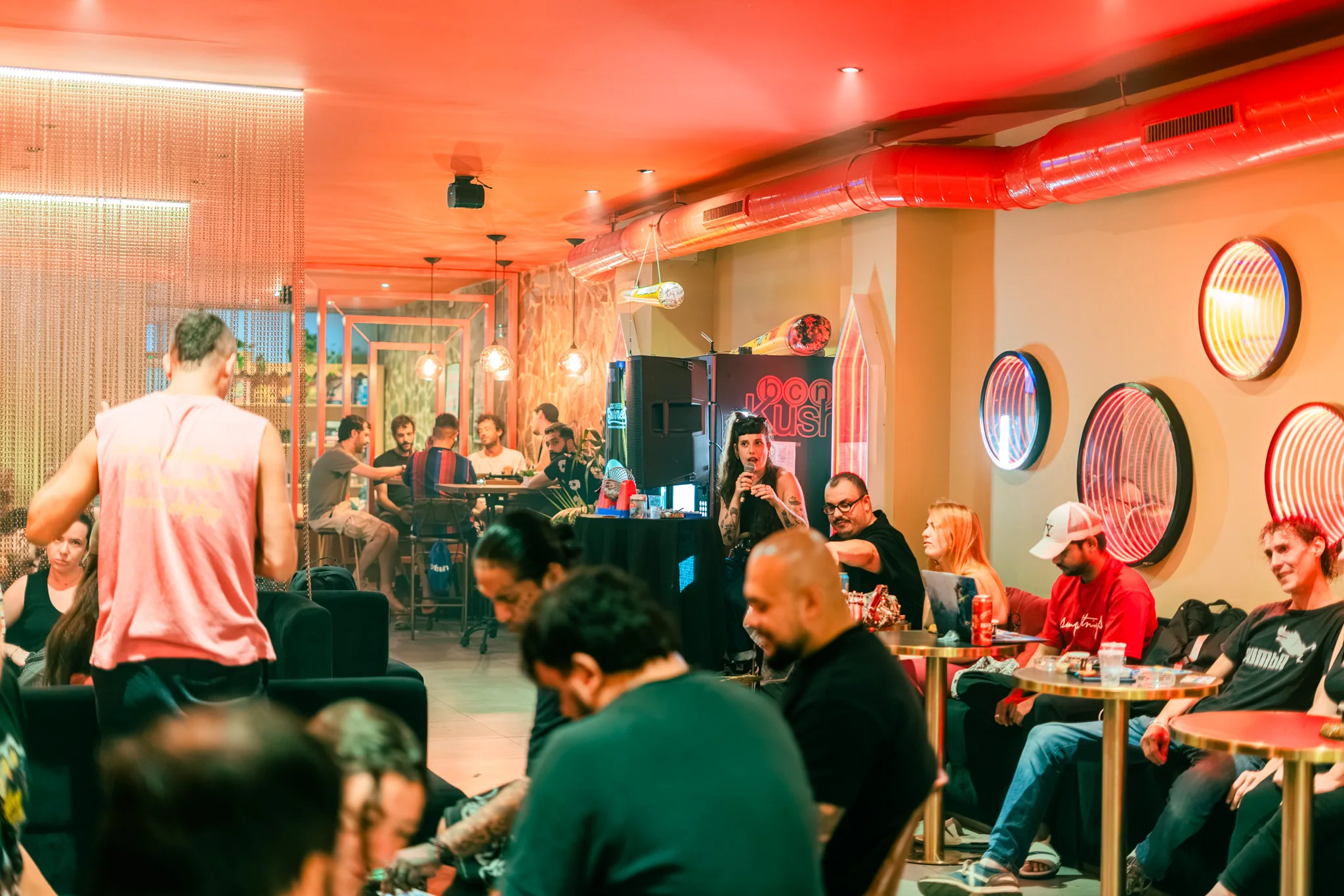 Sala principal de Bcn Kush Weed Club, club cannábico en Sants (Barcelona), con socios, luz cálida y espejos redondos