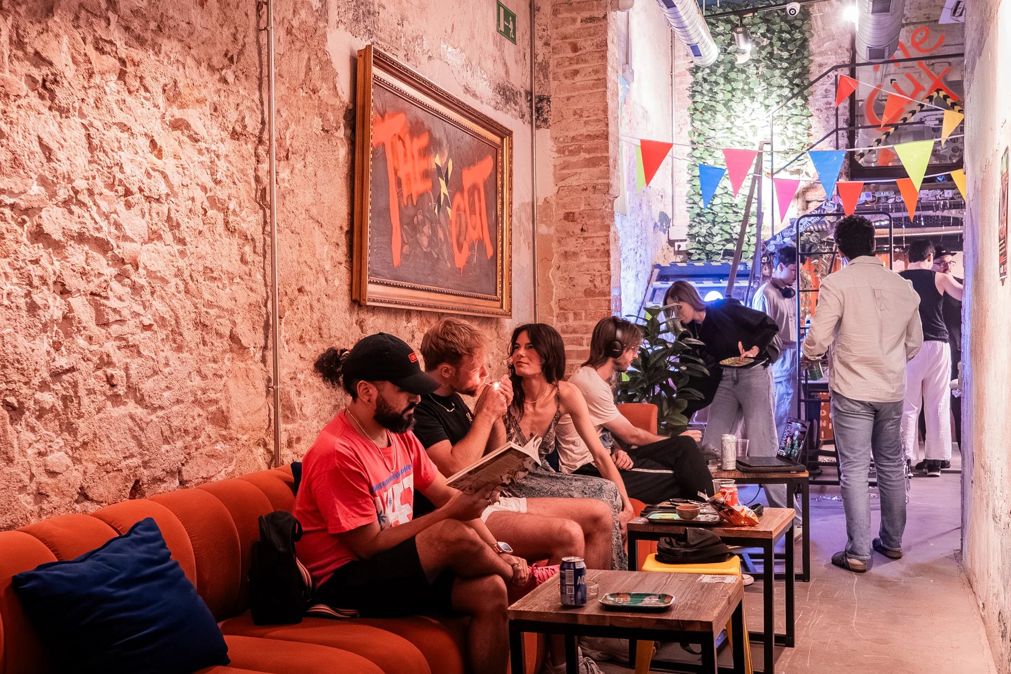 Sala principal de The Cut Weed Club, club cannábico en Sant Antoni (Barcelona): paredes de ladrillo, sofás naranjas y socios en las mesas