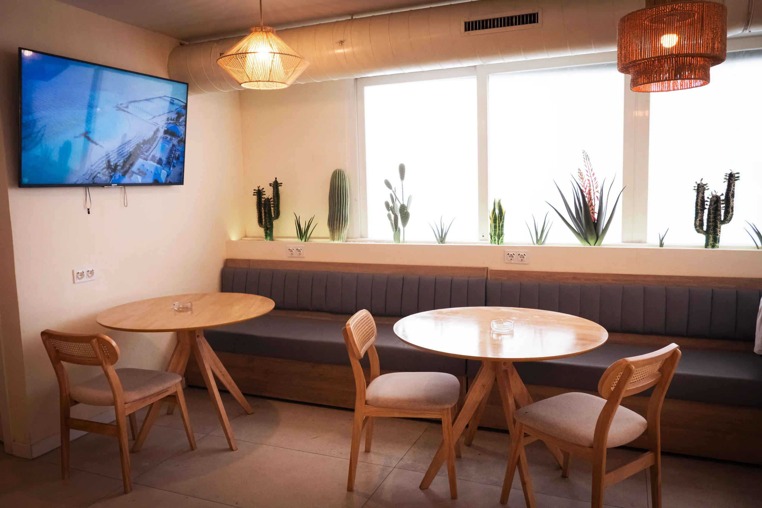 Sala principal de Zen Weed Club, club cannábico en Cala de Bou (Ibiza): banco corrido, mesas redondas de madera clara y lámparas de ratán